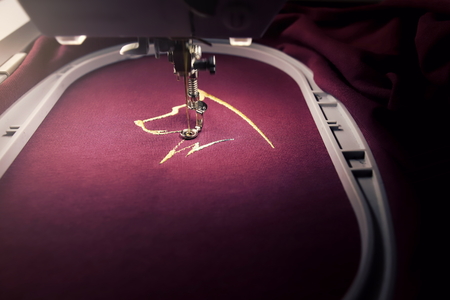 Embroidery with embroidery machine of dog head in gold on claret fabric - chinese new year concept - front view on stitching and hoop in bright luxurious vintage light mood - copy space for textの写真素材