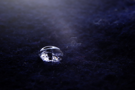close-up of sparkling drop of water on luminous dark blue boild wool - bright light mood with deep shadows - foreground and background blanked out blurryの写真素材