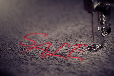 embroidery of red lettering SALE on soft grey fabric with embroidery machine - colored close up - background and foreground blanked out blurry - marketing and business conceptの写真素材