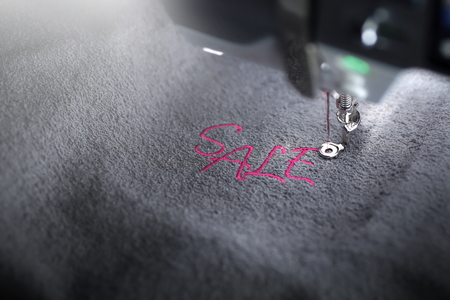 embroidery of pink lettering SALE on soft grey fabric with embroidery machine - top view on font and machine head - background and foreground blanked out blurry - marketing and business conceptの写真素材