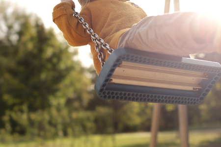 Child swinging on playground in bright afternoon sun - detail view underneath the swing seat - bright backlight - background blanked out blurryの写真素材