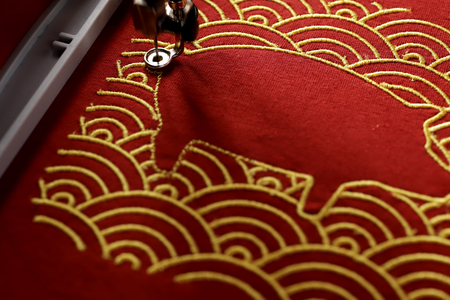 oblique view on pig embroidery framed by traditional shell pattern with gold on red fabric in...