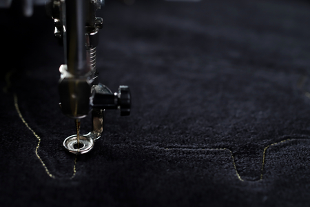 Detail view on embroidery machine stitching outline of a pig on black velvetely fabric in dark light...
