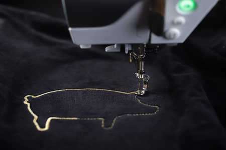 Tilted front view on embroidery machine stitching pig motive with gold yarn on black velvetely fabric - foreground and background blanked out blurryの写真素材