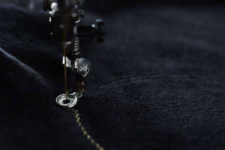 Detail view on needle of embroidery machine piercing in black velvetely fabric to stitch underlay of pig motive with gold yarn in dark light mood - Macro with blurred backgroundの写真素材
