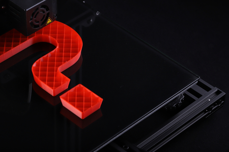 oblique top view on 3D-printer with big question mark made from red plastic - dark surrounding with...