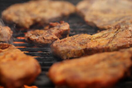 closeup on crispy grilled meat on smoking hot cast-iron grate with flames underneath- realistic food and barbecue party concept - foreground and background blanked out blurry の写真素材