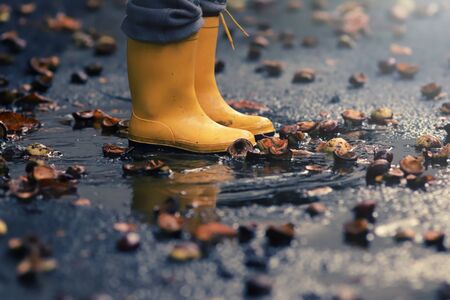 closeup on yellow rubber boots of a child in a puddle after a rain on a stormy autumn day - childhood and seasonal concept - background blanked out blurryの写真素材