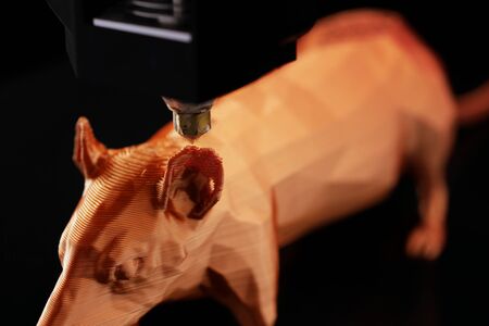 close up on ear of low poly rat sculpture being made by 3D printer from shiny orange filament in...