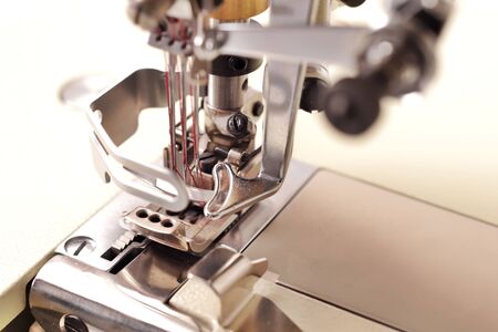 close up on needles of a solid industrial coverlock sewing machine with red thread - background...