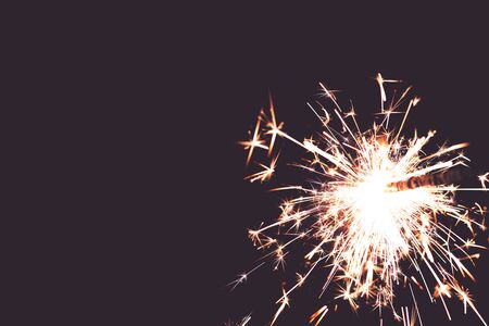 closeup view on burning sparkler in front of hazy toned black background - copy space for text