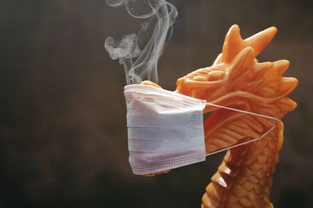 traditional golden chinese dragon sculpture with protective face mask and smoke from nostrils - side view on head with dark and blurred background - global epidemic conceptの写真素材