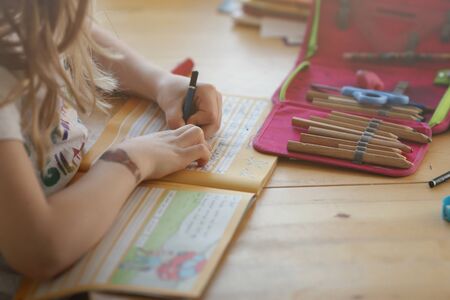 young blonde left-handed girl is writing in a workbook to train her handwriting at home - homeschooling conceptの写真素材