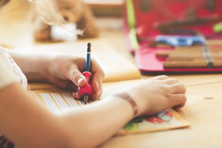 closeup on the hand of a young blonde left-handed girl training her handwriting at home in bright surrounding- homeschooling conceptの写真素材