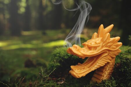 traditional golden chinese dragon sculpture with smoke curling frome nostrils stands in rich green forest scenery with blurred backgroundの写真素材