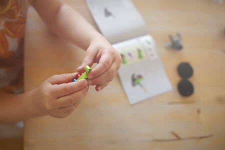 young girl in colorful dress puts togehter parts with her little fingers to build a toy tractor from...
