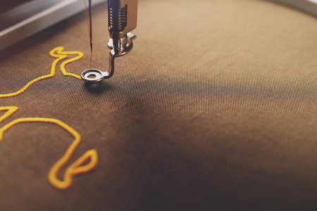 An ox symbol is stitched by an embroidery machine on shiny olive green fabric with golden yarn in...