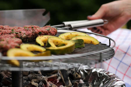 fresh kofta lamb meat spits and seasoned pumpking slices are grilled by a woman on a stainless steel charcoal grill - outdoor barbecue scenery with selective focusの写真素材