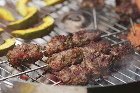 narrow closeup on fresh kofta lamb meat spits and pumpkin slices that are grilled on a charcoal grill - barbecue scenery with selective focusの写真素材