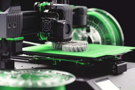 oblique view on FDM 3D printer with printed parts while manufacturing white helical gears. brightly...