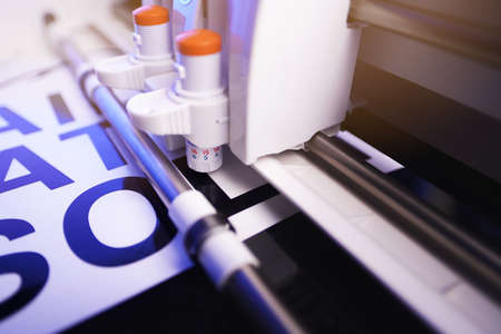 tool head of cutting plotter with adjustable blades. making of adhesive lettering from black vinyl foil in bright light. Side view with energetic blue light. selective focus. advertising conceptの写真素材