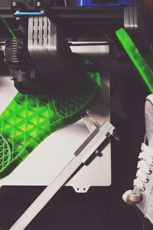 A shoe sole prototype with complex inner structure is printed from green plastic filament. matte style top view with gray sneaker shoes and calliper. Upright portrait orientation. selective focusの写真素材