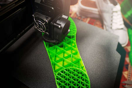 3D printer makes shoe sole with distinct inner structure from green plastic filament on black PEI...