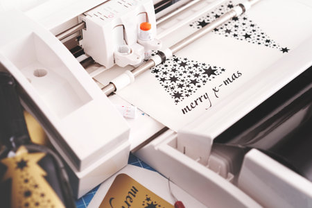 christmas stickers with lettering are cut from black adhesive vinyl film by a plotting machine. DIY and advertisement concept with tools, wine bottle and additional sticker. selective focusの写真素材