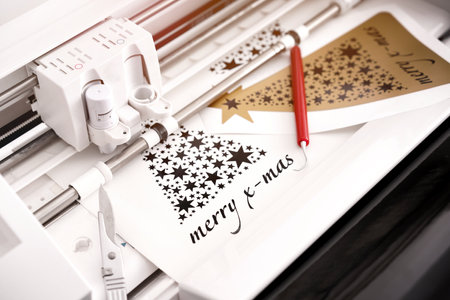 closeup view on machine head of plotting machine that cuts christmas sticker with lettering from black adhesive vinyl. DIY concept with tools and additional stickers. warm light mood. selective focusの写真素材