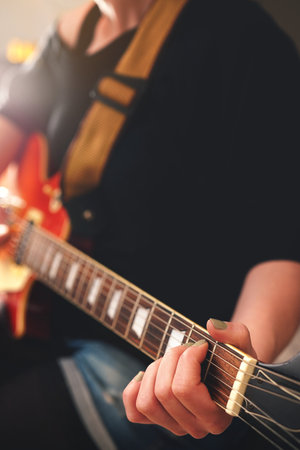 Woman grips chord on electric solidbody guitar with cherry sunburst body. Black shoulder top....