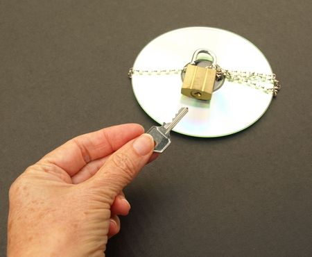 Photograph of hand holding a key and a CD with chain and padlock. Dark background.の写真素材