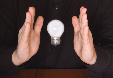 Flying electrical bulb between palmsの写真素材