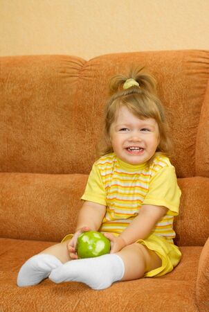 Small smiling girl in yellow with green appleの写真素材