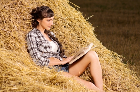 Young woman reading book on haystackの写真素材