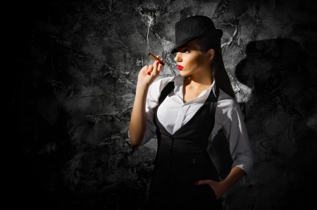 Dangerous and beautiful criminal girl with cigar on grey wallの写真素材