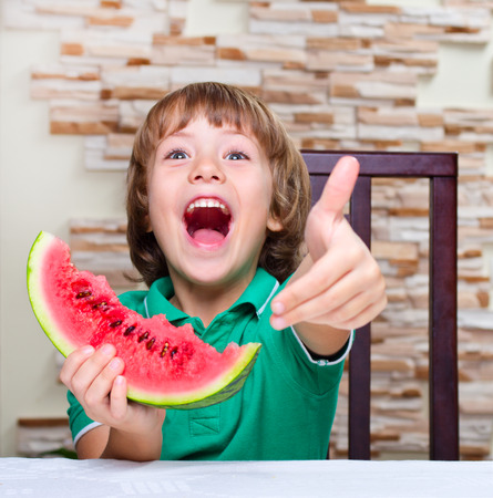 Little boy eating an watermelon at the tableの写真素材