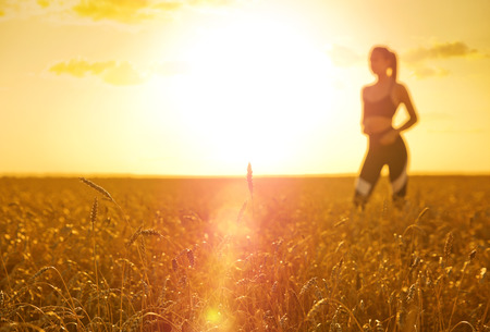 Sporty woman in wheat field at sunsetの写真素材