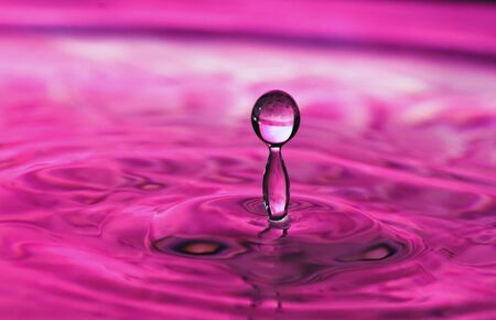 Water drop frozen in time with red reflection from colored background