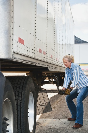 Pretty blonde woman truck driver cranking the dolly handle to raise the legs of a traier after backing her tractor under it.の写真素材