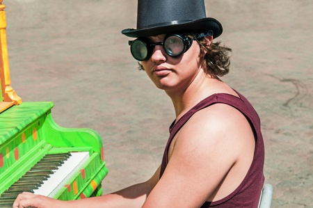 Youn man in a top hat and goggles playing a colorful piano outdoors.の写真素材