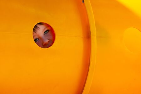 A Little boy peeking through a hole in the playground plastic tunnel he is crawiling in.の写真素材