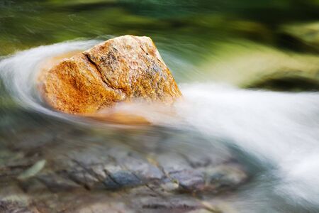 Red stone in a mountain flowing streamの写真素材