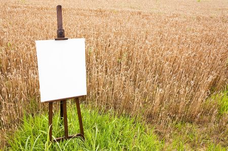 Blank canvas on a wooden easel over a grain field. Large copy space on the white canvas. Horizontal orientationの写真素材