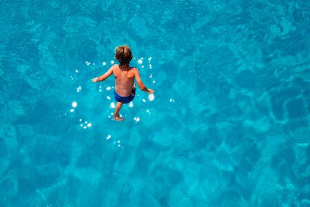 Blonde little boy jumping into the turquoise water of a tropical sea, rear view.の写真素材