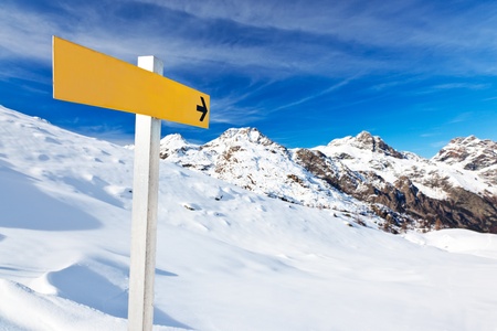 Yellow mountain guidepost along an alpine pathway over a snowy landscape in a clear winter day. Italian Alps, Val d'Aosta, Italy.の写真素材