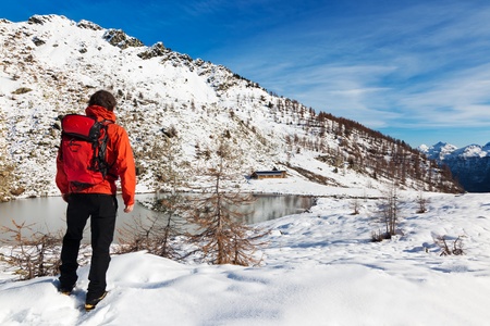 One man young male hiker stands in front of a alpine lake looking to the snowy landscape, rear view.の写真素材