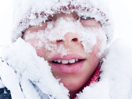Caucasian child looking at camera, covered with snow. Winter season.の写真素材