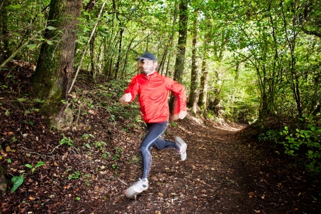 Male trail runner running in the forest on a trail. Red shirt and black pants. Summer season. Slight blur in runner to show motion. Horizontal composition.の写真素材