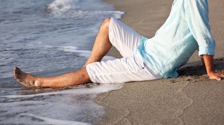 Caucasian young man, in casual clothing, sitting on beach in the sunrise light の写真素材