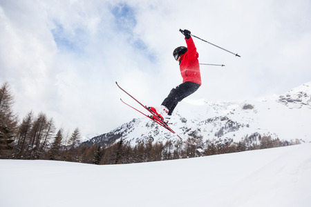 Male kid performs a high jump with the ski  Winter season, red jacket  Valle d